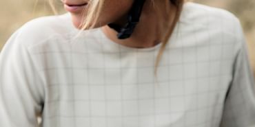 Eine Frau mit Helm und Sonnenbrille und Fahrradbekleidung der Marke Ortovox macht eine Pause auf einen Biketrail