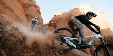 Ein Mann und eine Frau fahren auf Scott E-Bikes einen Trail in felsiger Landschaft hinunter