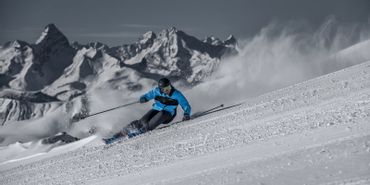 Ein Mann carved auf der Piste mit Stöckli Ski. Im Hintergrund ist ein winterliches Bergpanorama