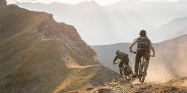 Two men bike on a trail on a ridge of a mountain