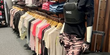 Eine große Auswahl an funktionaler Bekleidung und vielen anderen Accessoires zum Radfahren dekoriert an einer Wand im Check In Bikecenter Serfaus
