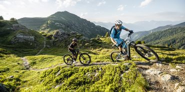 Ein Mann und eine Frau fahren auf Scott E-Bikes einen Trail in hügeliger Landschaft entlang