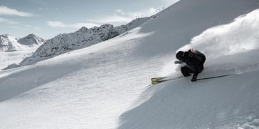 Ein Mann fährt im Gelände im Tiefschnee mit Kästle Ski einem Grat entlang