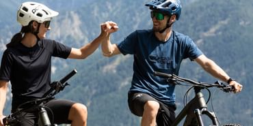 Eine Frau und ein Mann sitzen auf ihren E-Fully Mountainbikes mit Helm und Oakley Sonnenbrille auf und schauen in die Berglandschaft von Serfaus