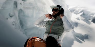 Ein Mann zieht sich am Berg kniend im Schnee seine Skiausrüstung an. Vor ihm steht ein Ortovox Tourenrucksack.