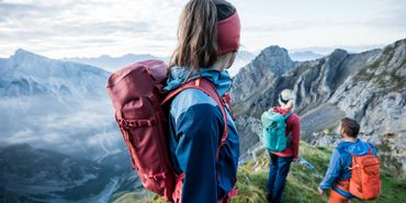 Eine Gruppe steht ausgestattet mit Wanderbekleidung von Ortovox an einem Berggrat und Blicken in das Bergpanorama mit hohen Gipfeln