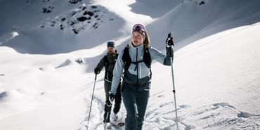 Zwei Tourengeher laufen mit Tourenski durch Pulverschnee einen Berghang hinauf