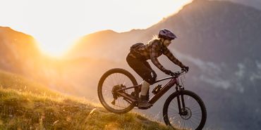 Eine Frau fährt auf einem Scott E-Mountainbiken einen Trail im Sonnenuntergang