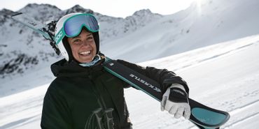 Eine Frau hat ihre Ski auf der Piste im Skigebiet geschultert und lächelt