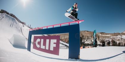 Anna Gasser jumped auf ein obsticle im Funpark mit einem Burton Snowboard. Im Hintergrund sind bereits frühlingshafte Berghänge