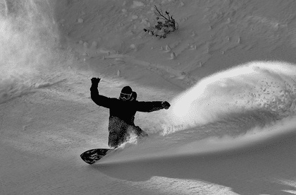 Egal ob Carving, Freeride oder beides - teste die neusten Boards der Saison Ein Snowboarder macht mit seinem Snowboard im tiefen Schnee im Gelände einen riesigen Spray