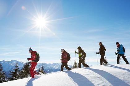 Ein Skilehrer geht mit einer Gruppe in Schneeschuhen in einer tief verschneiten Winterlandschaft im Hintergrund ist das Bergpanorama in Serfaus