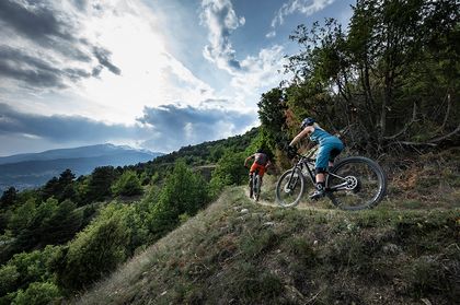 Ein Mann und eine Frau fahren auf Scott E-Bikes einen Trail in hügeliger Landschaft entlang
