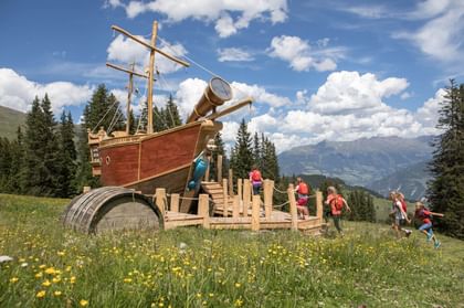 Eine Gruppe von Kindern klettert auf ein großes Piratenschiff aus Holz auf dem Wanderweg in Serfaus