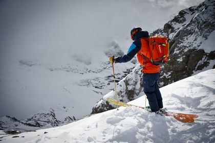 Ein Skifahrer steht mit einem ABS Lawinenrucksack von Scott auf Ski an einer Bergkante und blickt in die weiß verschneite Berglandschaft