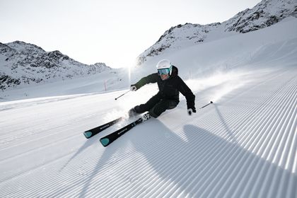 Ein Mann carved auf der Piste mit Kästle Ski. Im Hintergrund ist ein winterliches Bergpanorama 