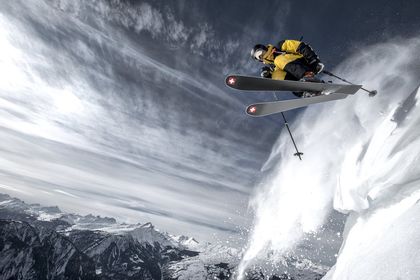 Ein Skifahrer springt mit Stöckli Ski von einer Schneekante in den Pulverschnee. Im Hintergrund ist eine winterliche Berglandschaft