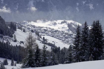 Winterliches Bergpanorama mit verschneiten Wiesen und Wäldern und Bergen. In der Mitte liegt Serfaus