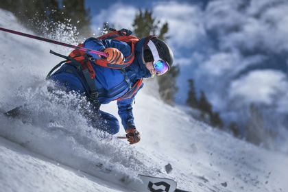 Eine Skifahrerin fährt mit ABS Rucksack einen tiefverschneiten Pulverschneehang hinunter