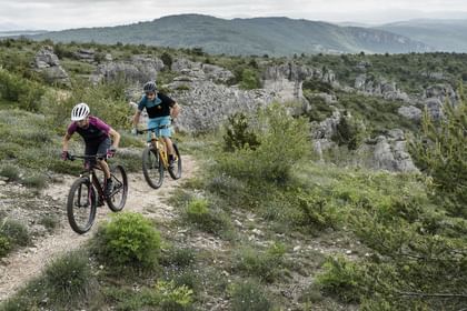 Ein Mann und eine Frau fahren auf Scott E-Bikes einen Trail in hügeliger Landschaft entlang