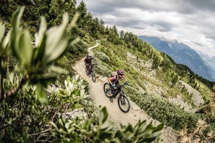 Ein Mann und eine Frau fahren auf Scott E-Bikes einen Trail in hügeliger Landschaft entlang