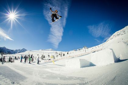 Ein Snowboarder springt über ein Gap und macht dabei einen Grap im Funpark von Serfaus