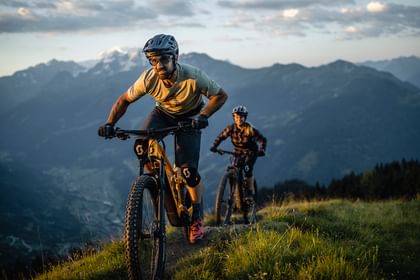 Ein Mann und eine Frau fahren auf Scott E-Bikes einen Trail in hügeliger Landschaft entlang