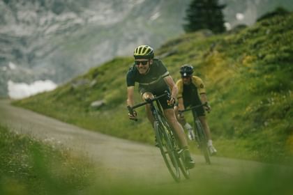 Zwei Männer fahren mit Scott Addict Gravelbikes eine Straße entlang im Hintergrund ist eine Berglandschaft