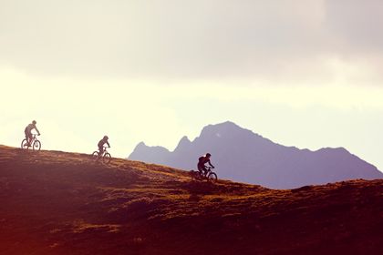 Eine Gruppe fährt auf Mountainbikes einen Bergtrail in Serfaus-Fiss-Ladis im Sonnenuntergang
