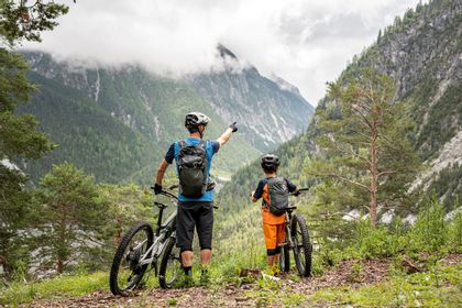 Ein Mann und ein Junge stehen mit ihren Scott Mountainbike und blicken auf eine Berglandschaft mit hohen Gipfeln