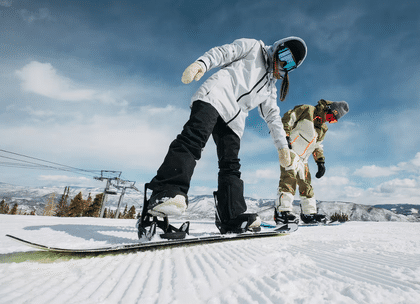 Eine Frau und ein Mann steigen mit ihren Step On Boots in die Burton Step on Bindung auf einer Piste im Skigebiet ein