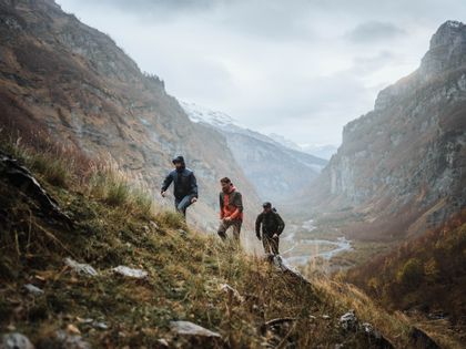 Eine Gruppe von Wanderern läuft in Scott Outdoor Bekleidung eine Wiese in einer rauen Berglandschaft