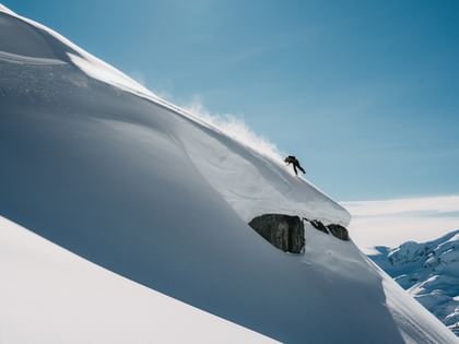 Ein Snowboarder springt im Gelände im Tiefschnee hoch über eine Kante 