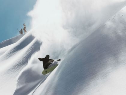 Ein Snowboarder fährt im Tiefschnee einen Berghang hinunter und hinterlässt einen Pulverschnee Spray