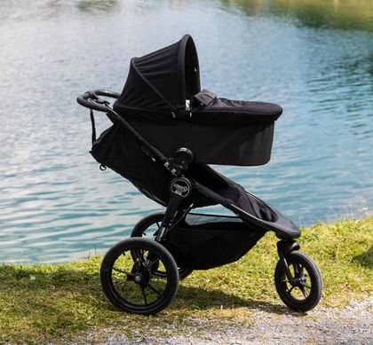 Summit Kinderwagen mit Babyschale auf einer Wiese im Hintergrund sind der Högsee, das Seeufer und Berge