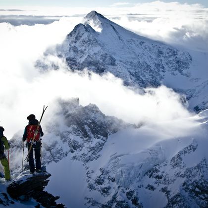 Zwei Tourengeher stehen oben auf einem Gipfel und schauen in ein winterliches Bergpanorama