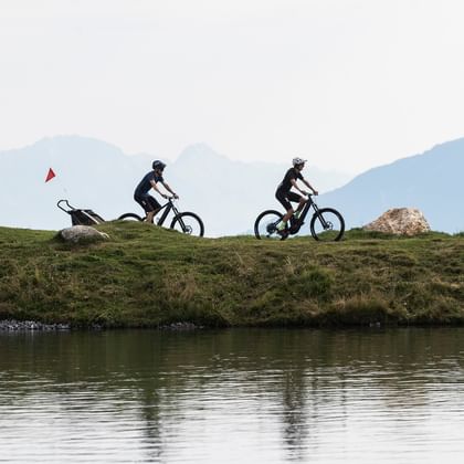 Eine Familie fährt mit einem E-Bike und Radanhänger entlang der Uferpromenade am Hög See Serfaus