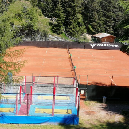 Ein Tennisplatz umgeben von Wald und ein Riesentrampolin im Vordergrund