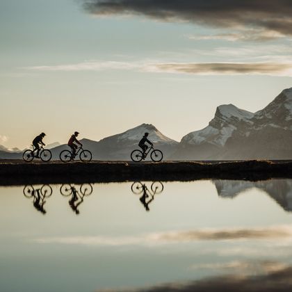 Eine Gruppe von Bikern fährt auf Mountainbikes an einem Bergsee entlang