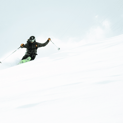 Eine Freeriderin fährt im tiefen Pulverschnee einen steilen Hang im Skigebiet hinunter