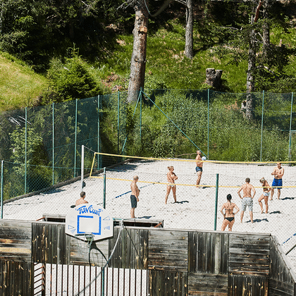 Neben einer Waldwiese spielt eine Gruppe von Personen auf dem Beachvolleyballfeld in Serfaus