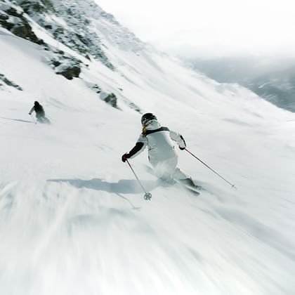 Eine Freeriderin und ein Freerider fahren im tiefen Pulverschnee einen steilen Hang hinunter.