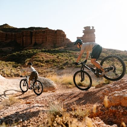 Ein Mann und eine Frau fahren auf E-Fully Mountainbikes der Marke Scott einen Weg in einer sommerlichen Berglandschaft rauf