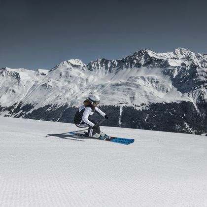 Eine Skifahrerin carved auf der Piste mit Stöckli Ski. Im Hintergrund ist ein winterliches Bergpanorama