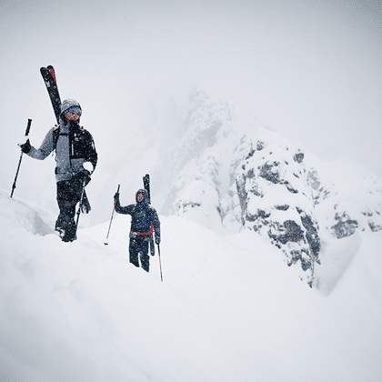 Eine Gruppe von Skifahrern geht eine Tour einen Berggrat hinauf, die Ski sind am Rucksack befestigt im Hintergrund ist eine Bergpanorama mit verschneiten Gipfeln