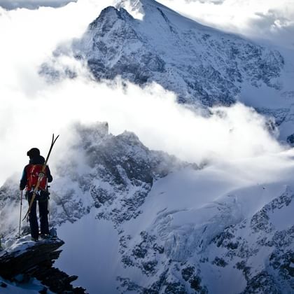 Zwei Tourengeher stehen oben auf einem Gipfel und schauen in ein winterliches Bergpanorama