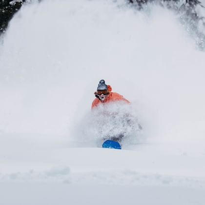Ein Mann fährt in verschneiter Berglandschaft im Tiefschnee mit einem Snowboard 