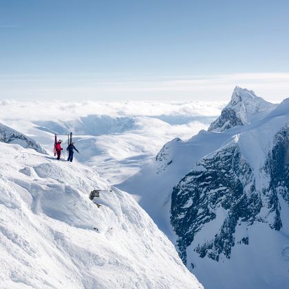 Zwei Skifahrer stehen am Gipfel und blicken in ein tiefverschneites, hochalpines Bergpanorama