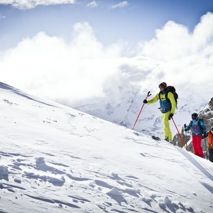 Eine Gruppe von Tourengehern laufen mit Tourenski einen Berghang hinauf