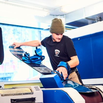 Servicemitarbeiter serviciert ein Snowboard an der Maschine in Handarbeit<br/>